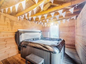 A wooden cabin interior with a hot tub, wooden walls, and a ceiling with triangular banners.