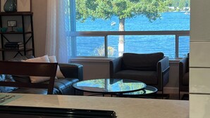 Eine moderne Küche mit einem großen Fenster mit Blick auf ein Gewässer, einem Essbereich mit einem Glastisch und einer Sitzecke mit Aussicht.