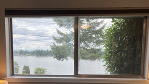 Ein Bett mit zwei Kissen, auf denen „Lake life“ steht, und ein Fenster mit Blick auf einen See und Bäume.