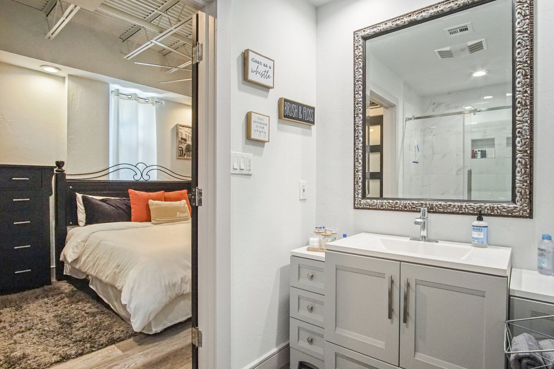 A bedroom with a bed, a dresser, a mirror, and a bathroom visible through an open door.