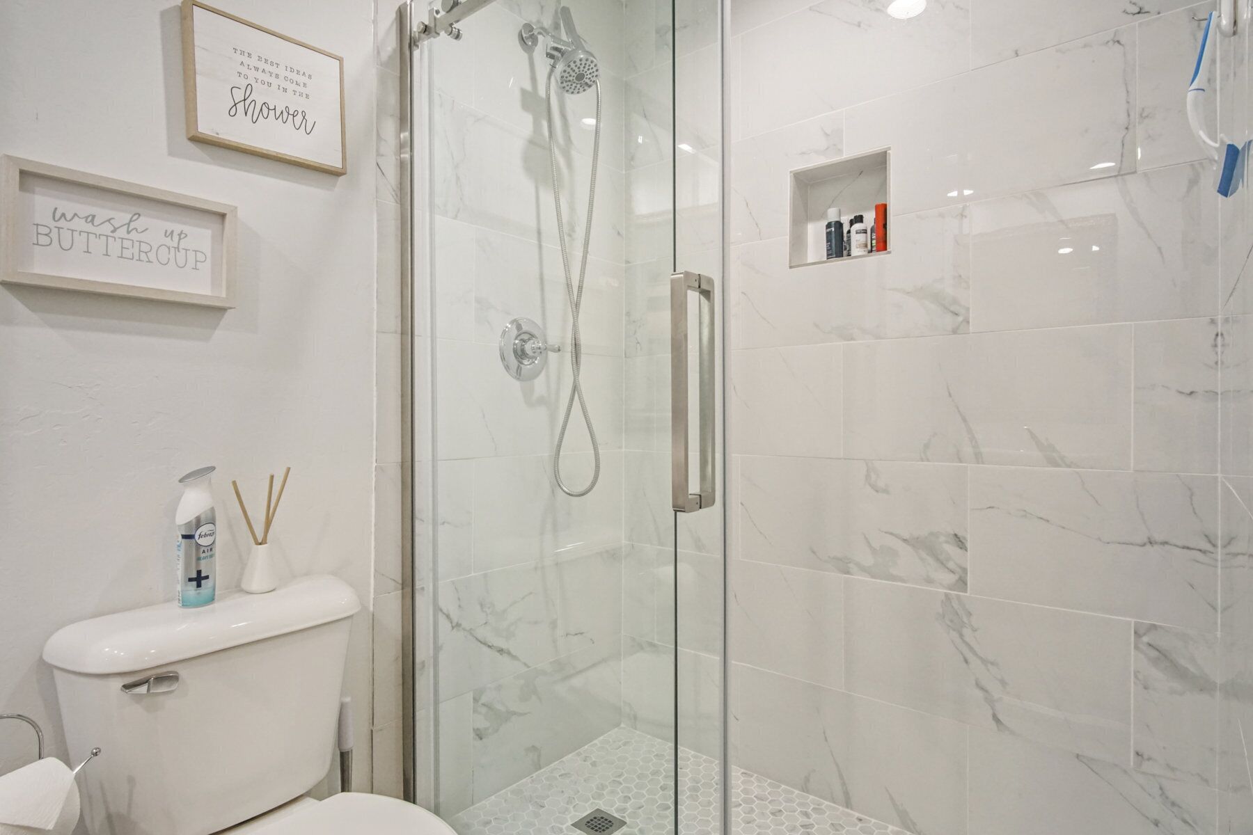 A modern bathroom with a glass-enclosed shower, marble tiles, and a toilet with a toilet paper holder.