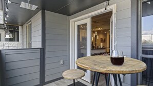 Eine kleine Terrasse mit einem runden Holztisch und zwei Hocker, ein Glas Rotwein und Blick in die Küche.