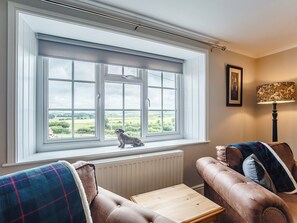 Ein Zimmer mit großem Fenster, einem Heizkörper, einem braunen Ledersofa, einem Holztisch und einer Lampe.