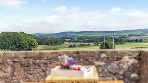 Un banc en bois avec une table en premier plan, offrant une vue panoramique sur un paysage pittoresque composé de collines et de champs vallonnés.