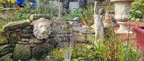 Un jardin agrémenté d’une fontaine en pierre, d’une statue et de diverses plantes.