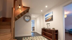 A spacious hallway with a wooden staircase, a patterned rug, a heart-shaped mirror, and a painting on the wall. - Amroth Holiday home with Sea Views (Narberth)