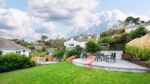 A backyard with a grassy lawn, a patio with outdoor furniture, and a wooden fence. - Amroth Holiday home with Sea Views (Narberth)