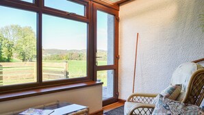 Une pièce dotée de grandes fenêtres, d’un fauteuil en osier et d’une table en verre.
