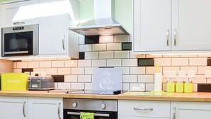 Une cuisine avec des meubles blancs, un four à micro-ondes, un grille-pain et un panneau indiquant : « Faites vos achats comme si le temps pressait. »