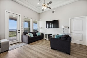 Relax in this spacious living room with a large sliding door leading to an outdoor area, a ceiling fan, and a flat-screen TV.