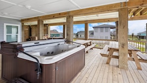En træterrasse med jacuzzi, picnicbord og træbjælker.