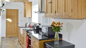 A kitchen with wooden cabinets, a black countertop, a stove, and a vase with flowers.