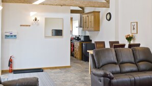 A living room with a leather sofa, wooden beams, a kitchen area, and a fire extinguisher.