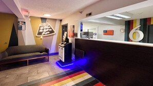 Een hotel lobby met een receptiebalie, een bank, een neonbord en een kleurrijk gestreept tapijt.