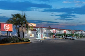A motel with a red roof sign, a parking lot, and a two-story building with balconies.
