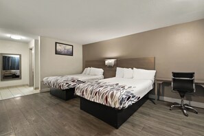 Ein Hotelzimmer mit zwei Betten, einem Schreibtisch, einem Stuhl und einem durch eine offene Tür einsehbarer Badezimmer.