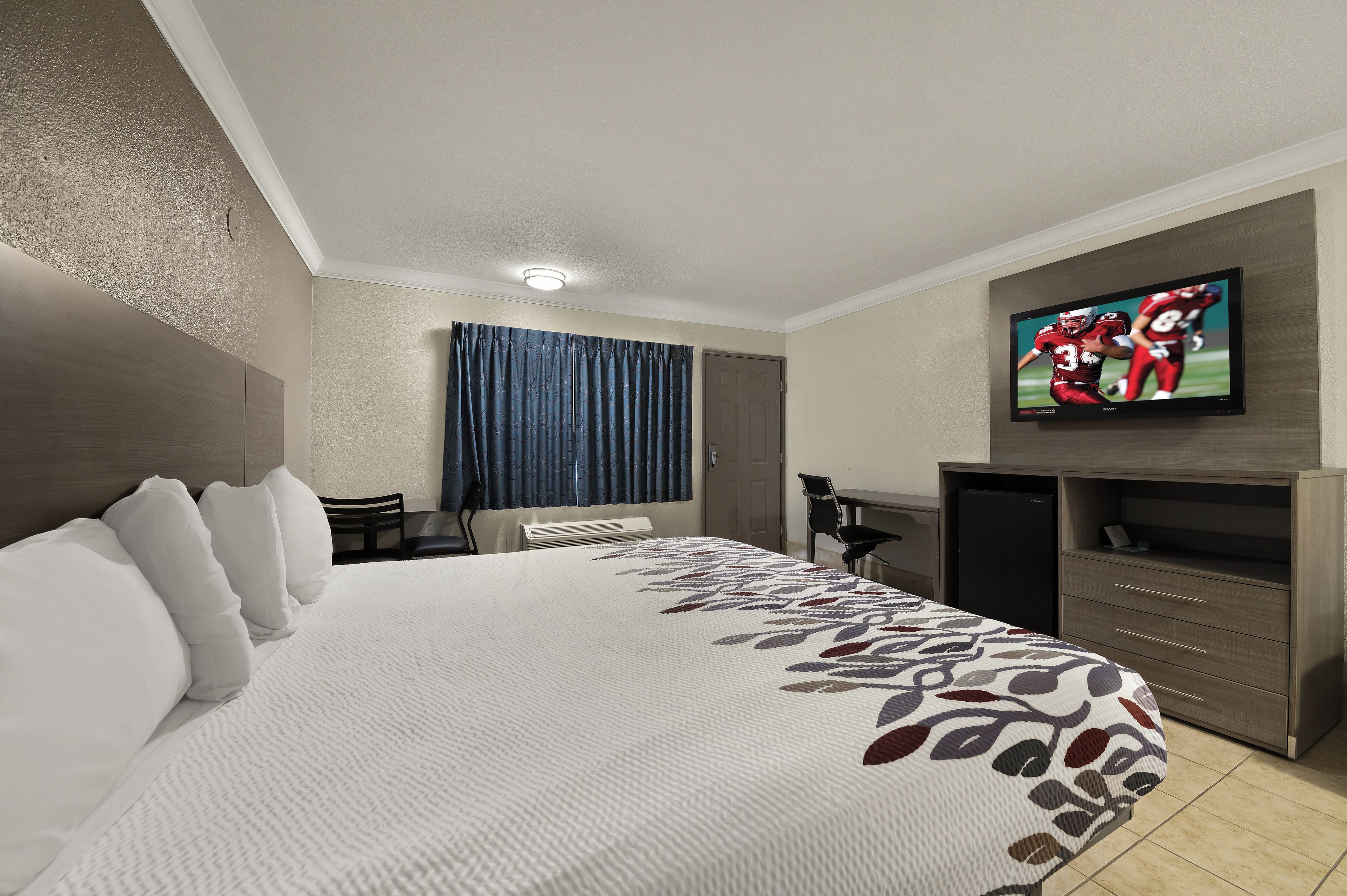 A hotel room with a large bed, a desk, a chair, a television, and a wardrobe.