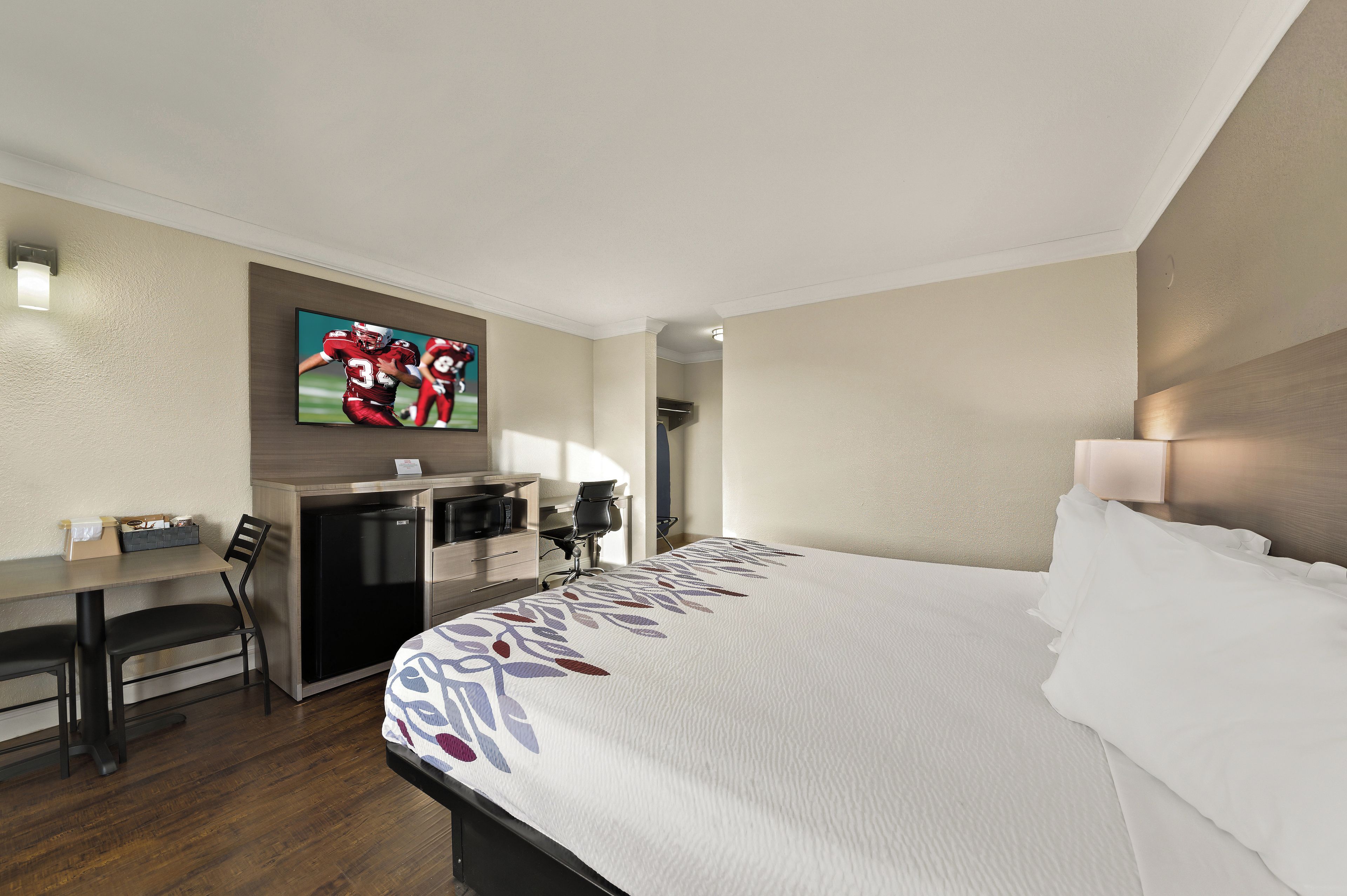 Habitación de hotel con cama, escritorio, silla, refrigerador, microondas y televisor en la pared.