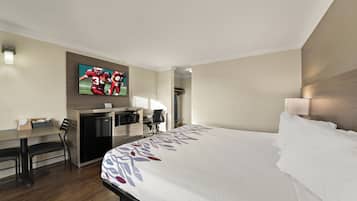 Habitación de hotel con cama, escritorio, silla, refrigerador, microondas y televisor en la pared.