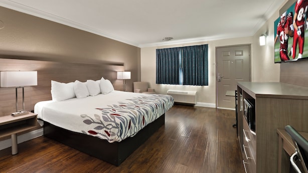 A hotel room with a large bed, bedside tables, a desk, a chair, a window with curtains, and a TV mounted on the wall. - Red Roof Inn Los Angeles – Bellflower (Bellflower)