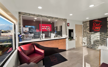 A reception area with a Red Roof Inn sign, a reception desk, a red chair, and a view of the street outside.