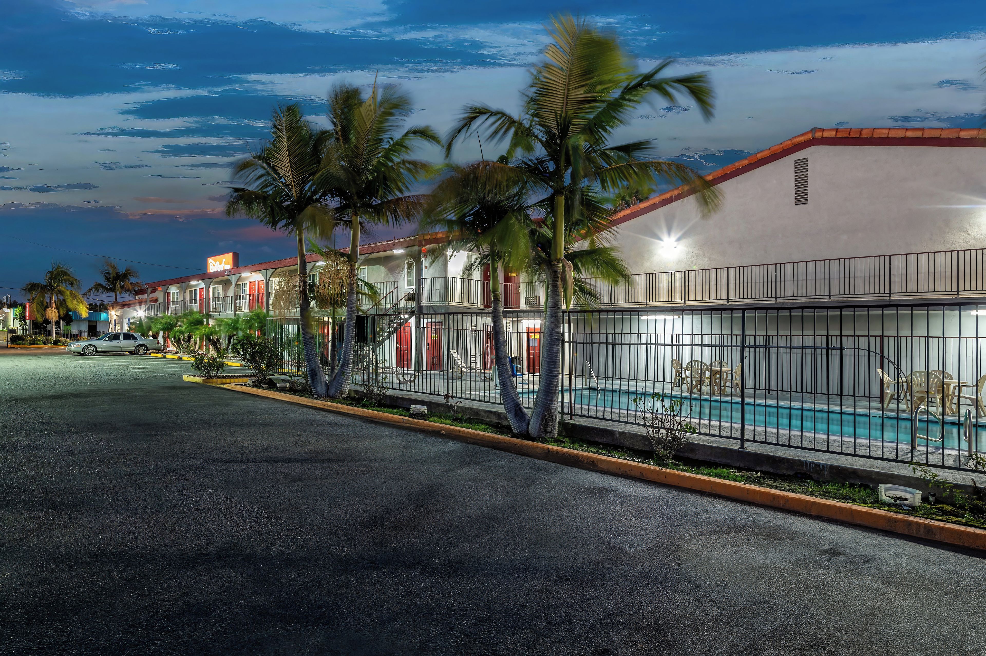 A hotel with a swimming pool, palm trees, and a street view.