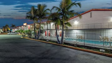 A hotel with a swimming pool, palm trees, and a street view.