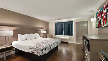 A hotel room with a large bed, bedside tables, a desk, a chair, a window with curtains, and a TV mounted on the wall.
