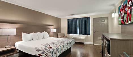A hotel room with a large bed, bedside tables, a desk, a chair, a window with curtains, and a TV mounted on the wall.
