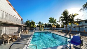 A swimming pool with clear blue water, surrounded by lounge chairs and a table. - Red Roof Inn Los Angeles – Bellflower (Bellflower)