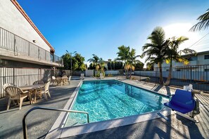 A swimming pool with clear blue water, surrounded by lounge chairs and a table. - Red Roof Inn Los Angeles – Bellflower (Bellflower)