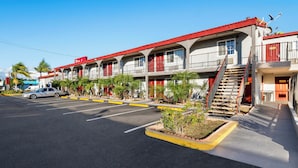 A motel with multiple balconies, a parking lot, and a clear blue sky. - Red Roof Inn Los Angeles – Bellflower (Bellflower)