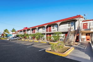 A motel with multiple balconies, a parking lot, and a clear blue sky. - Red Roof Inn Los Angeles – Bellflower (Bellflower)