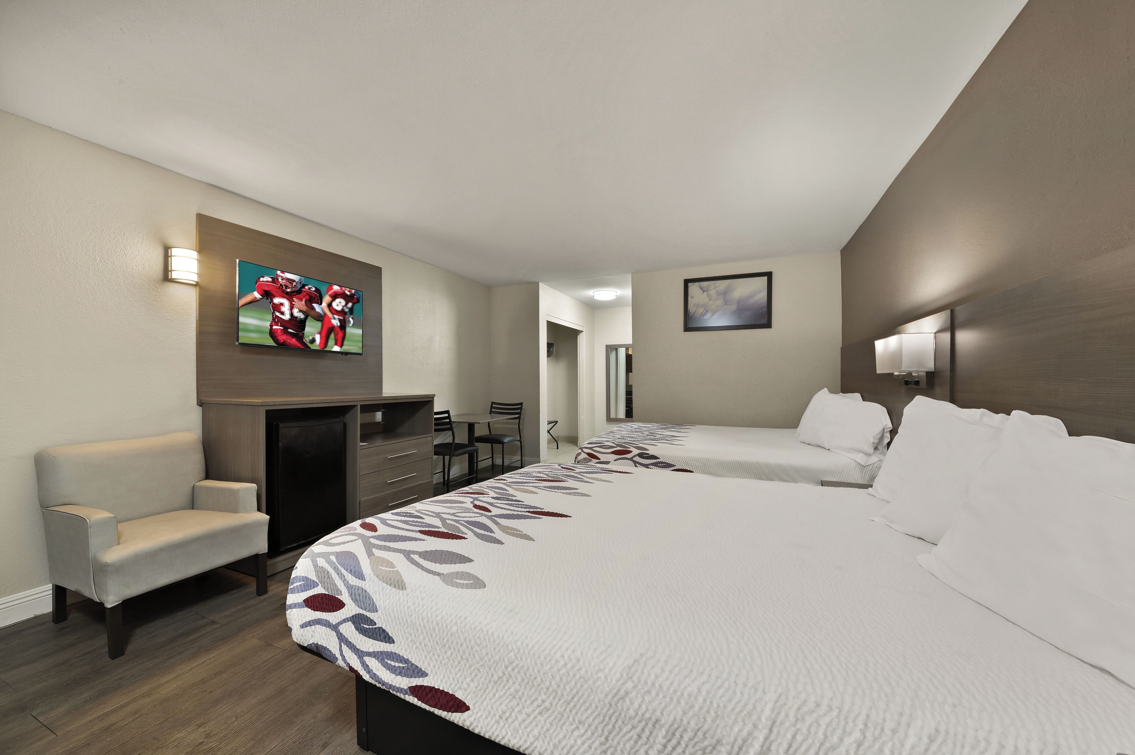 Ein Hotelzimmer mit Bett, Schreibtisch, Stuhl und einem an der Wand montierten Fernseher.