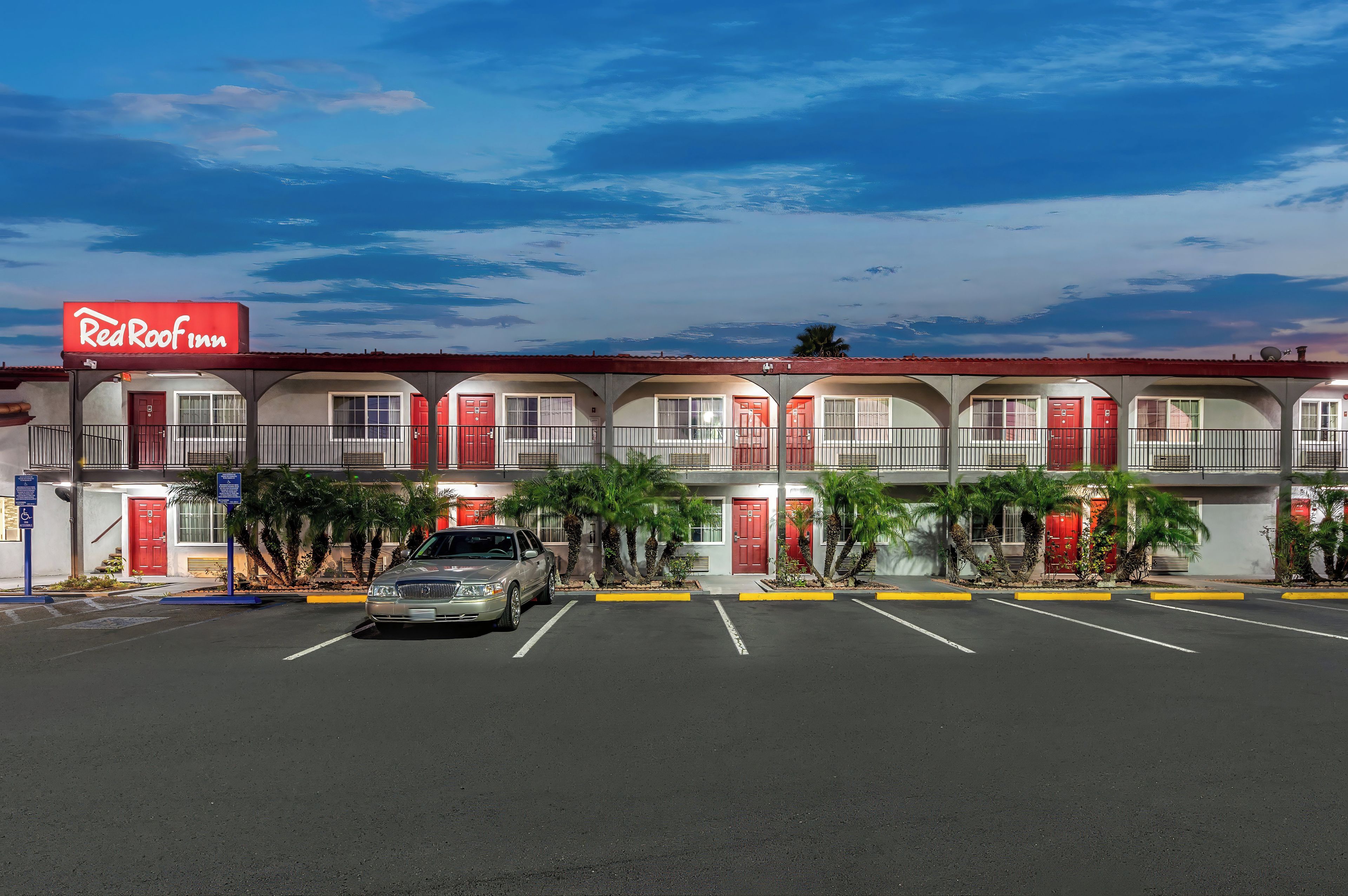Un Red Roof Inn con varios cuartos, un estacionamiento y cielo despejado.