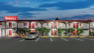 Un Red Roof Inn con varios cuartos, un estacionamiento y cielo despejado.