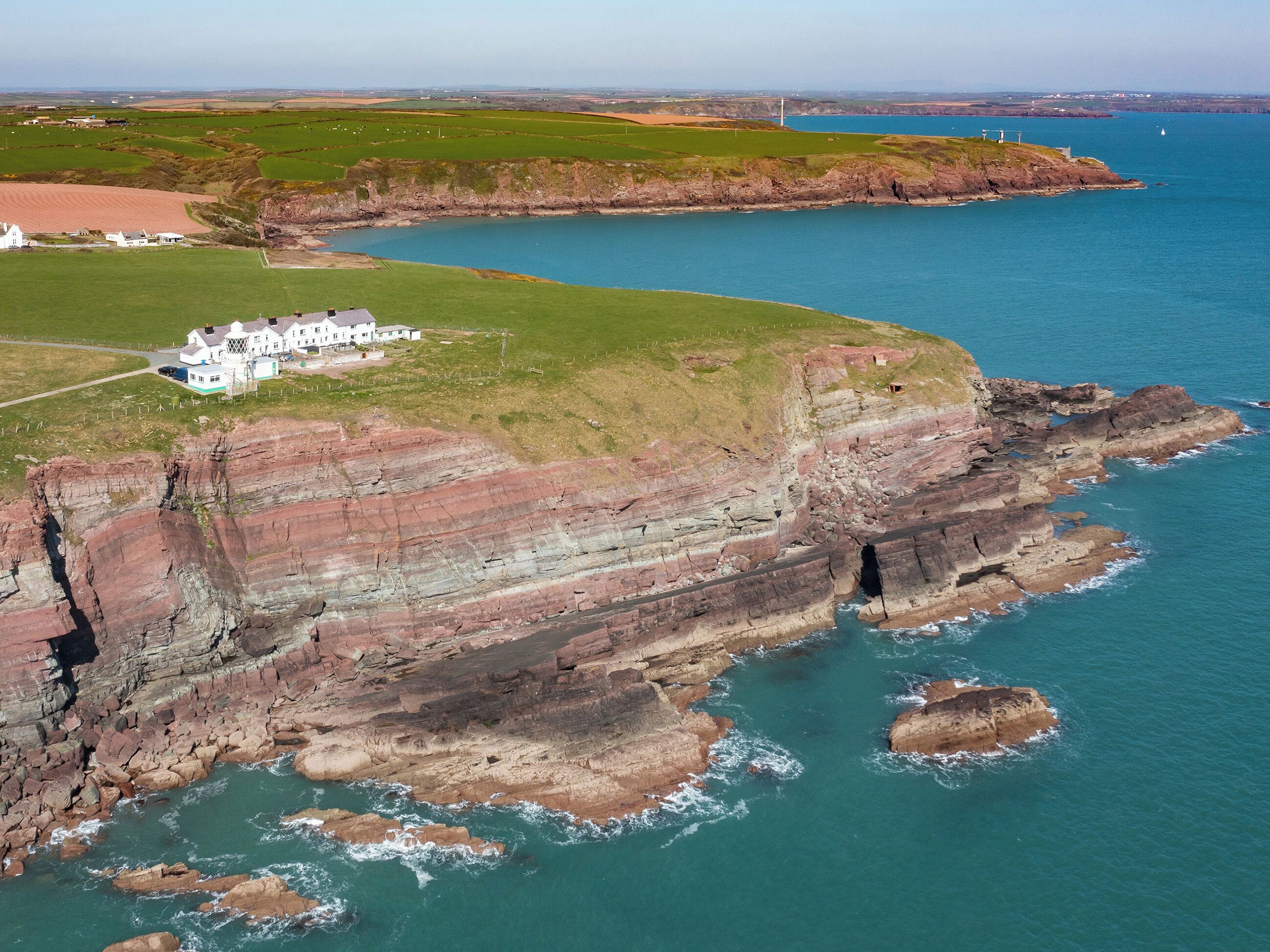 A coastal property with a large white building, rocky cliffs, and a view of the sea.