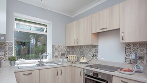 A modern kitchen with light wood cabinets, a Bosch oven, and a window with a view of greenery.