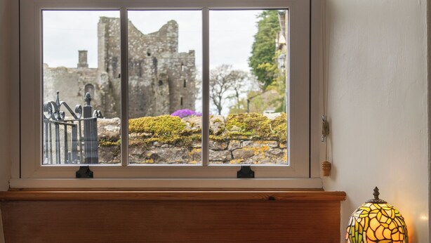 A window with a view of a castle, a lamp, and an open book on a wooden ledge.