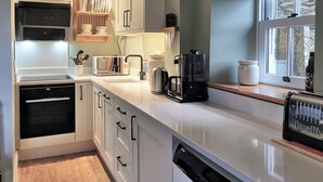 A modern kitchen with white cabinetry, a built-in oven, a coffee maker, and a dishwasher.