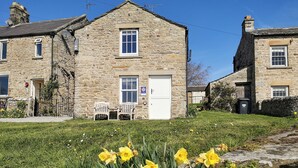 A stone building with a white door and windows, a small garden with yellow flowers, and a clear blue sky.