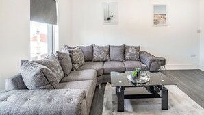 Ein modernes Wohnzimmer mit einem Ecksofa, einem Glastisch und Kunstwerken an den Wänden.