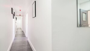 Ein schmales Entree mit Holzboden und weißen Wänden. An der linken Wand befinden sich gerahmte Bilder und an der rechten Wand ein großer Spiegel.