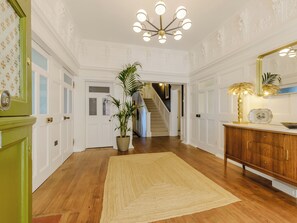 A hallway with a wooden floor, a beige rug, a green door, a white door, a staircase, and a wooden cabinet with a mirror.