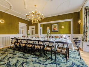 A dining room with a long table set for a meal, chairs, a chandelier, and a framed picture on the wall.