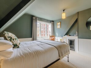 A bedroom with a bed, a window, a fireplace, and a mirror.
