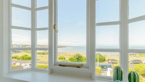 Une fenêtre donnant sur une plage et sur des bâtiments situés au loin.