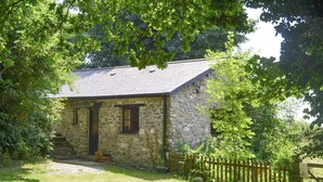 A stone cottage with a wooden door, a small porch, and a wooden fence.