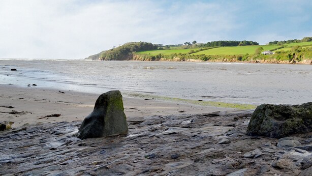A beach with large rocks and a grassy hill in the background.