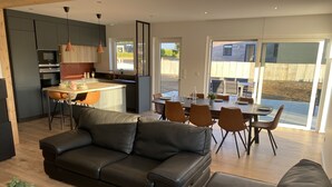 A modern living room with a black leather sofa, a dining area with a table set for four, and a kitchen with dark cabinets and a wooden island.